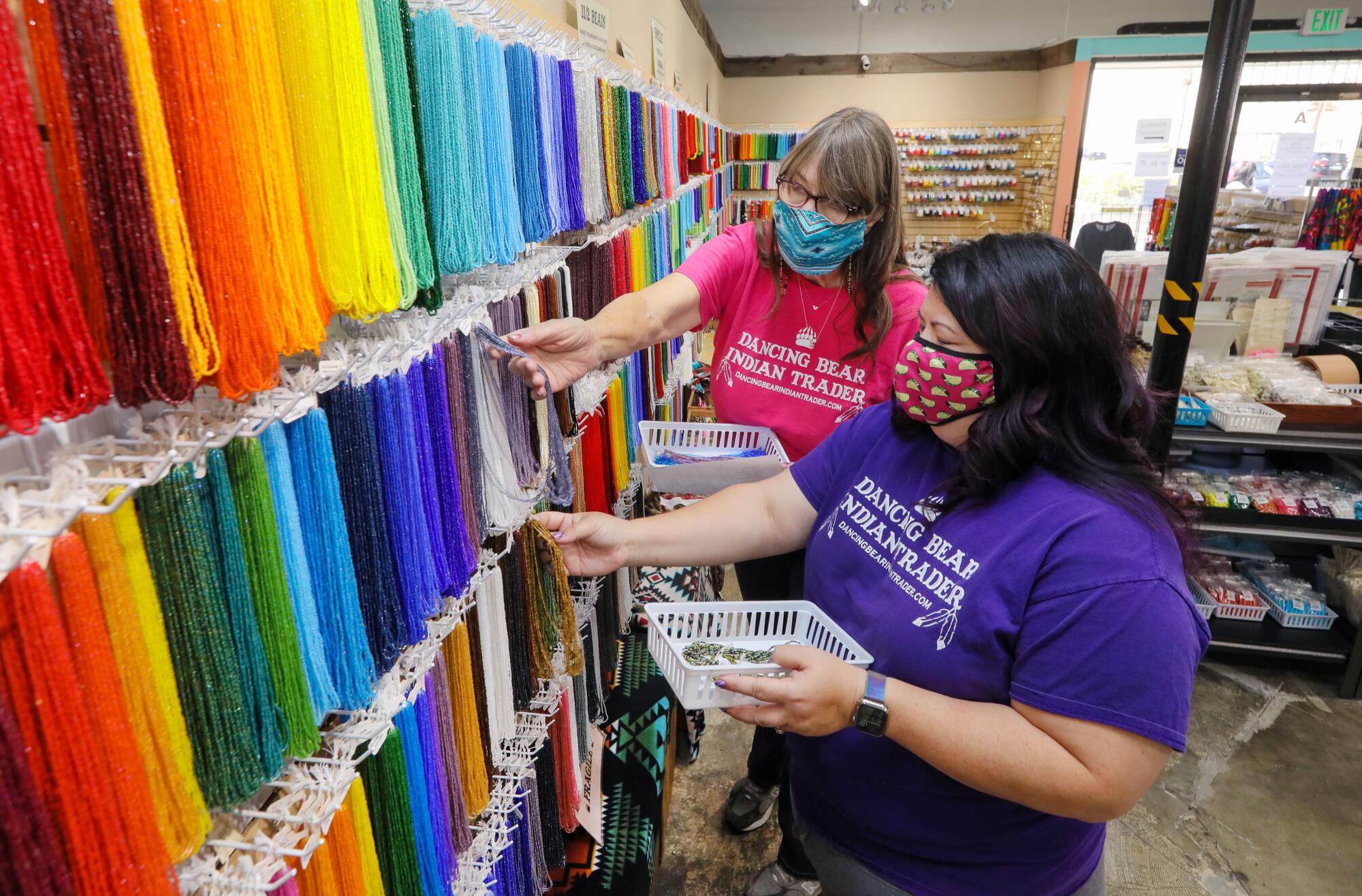 Chris Tracy and her daughter Svea Komori-Ang choose beads from a wall of hanging strings of beads of many colors