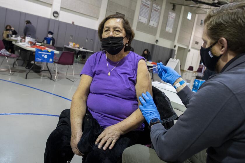 SANTA ANA, CA - MARCH 15: EMT specialist Andrew Roberts, right, give Eloisa Campos, 70, a Covid-19 vaccination in the gym at Villa Intermediate School on Monday, March 15, 2021 in Santa Ana, CA. (Brian van der Brug / Los Angeles Times)
