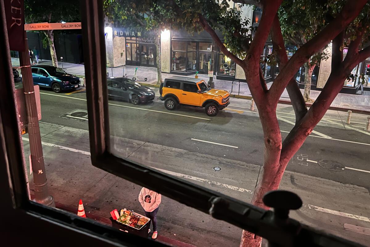 The view through an open window: parked cars and a hotdog stand.