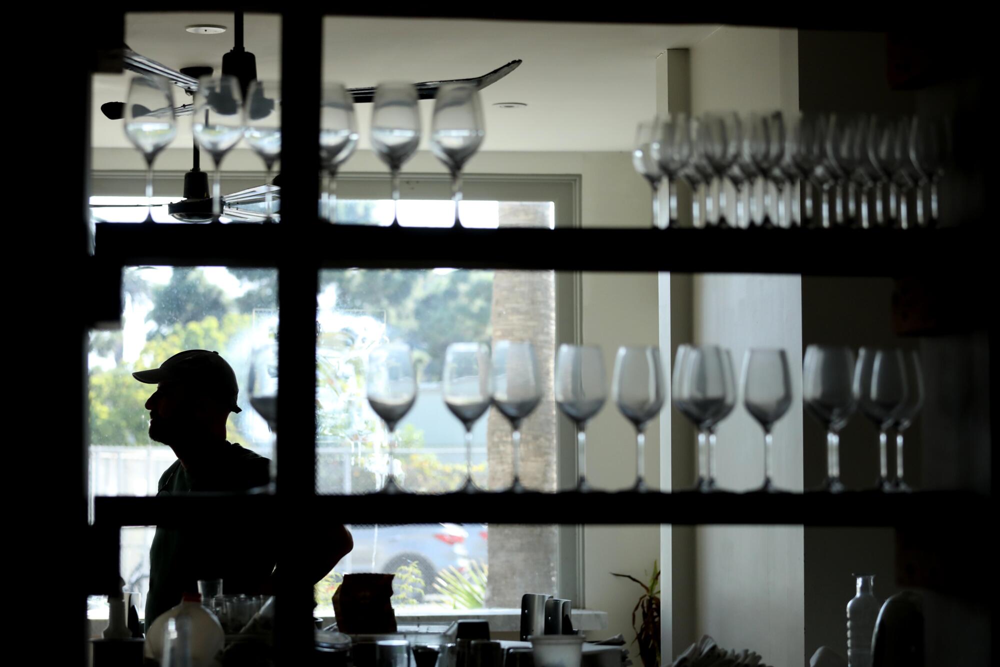A person in silhouette behind a shelf of wine glasses.