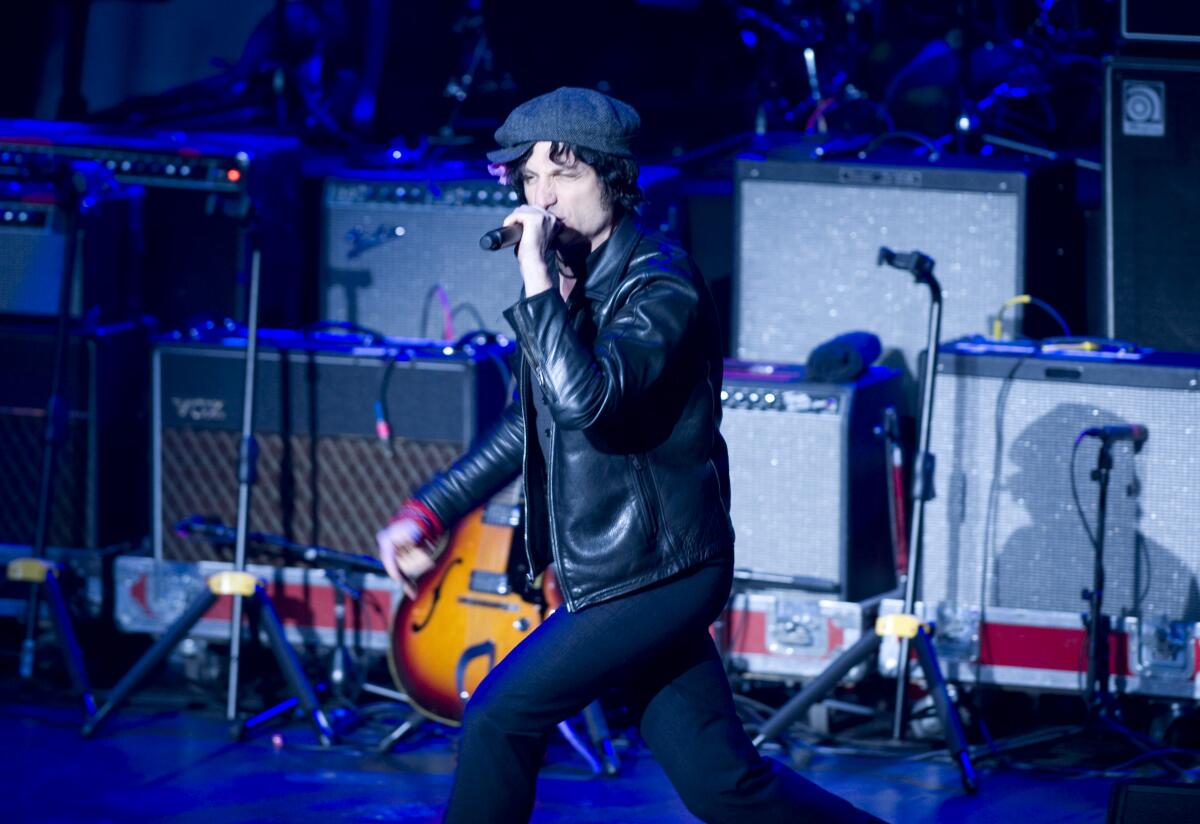 Jesse Malin strutting on stage with a microphone in his hand while wearing a black leather jacket and hat. 