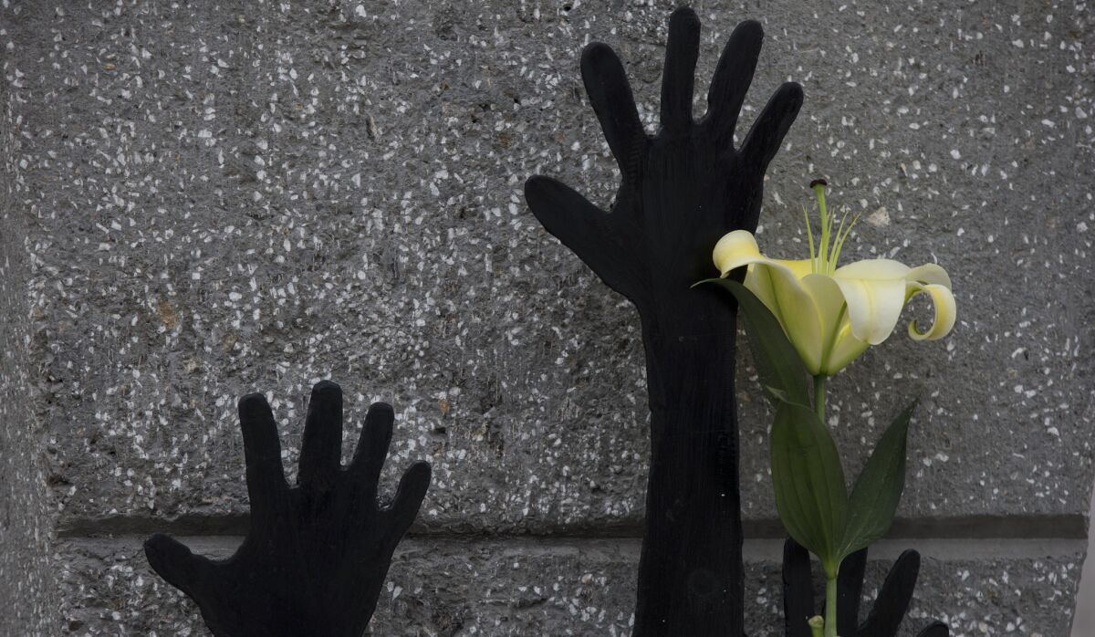 A flower rests next to hands reaching upward on a newly erected monument for students killed on the day 43 others disappeared just over a year ago.