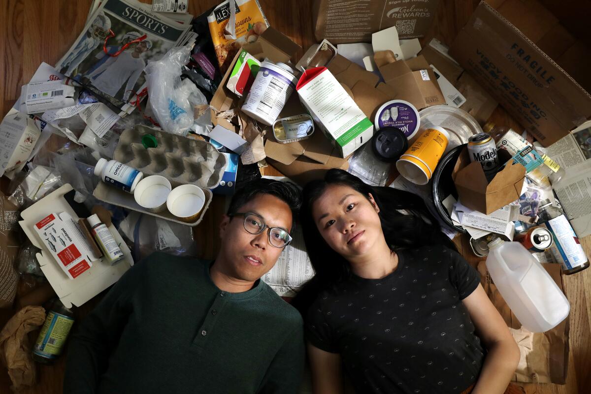 A couple lies down among a sea of recyclable and non-recyclable trash inside their home.