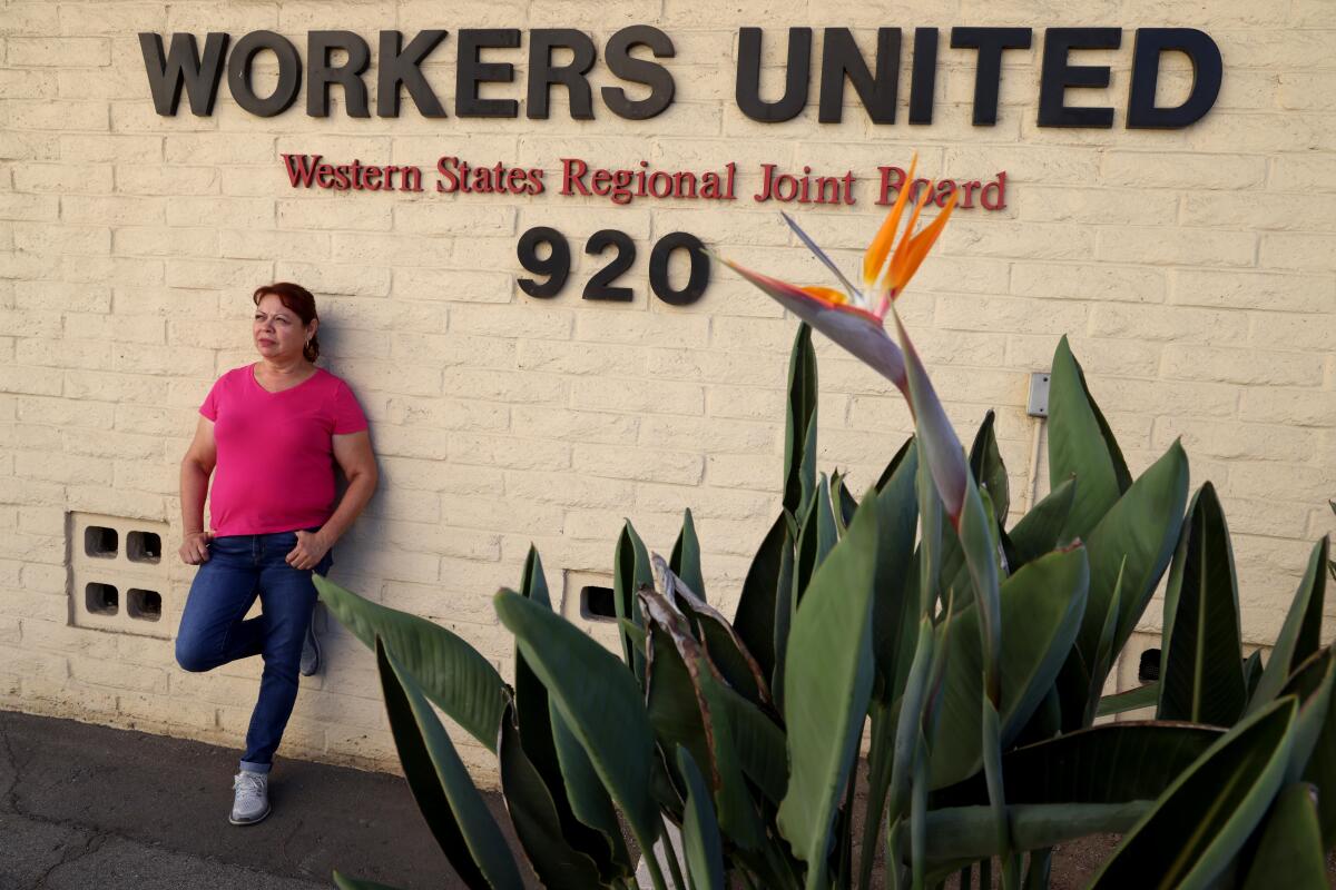 A woman in pink T-shirt and jeans leans against a wall with lettering touting Workers United 