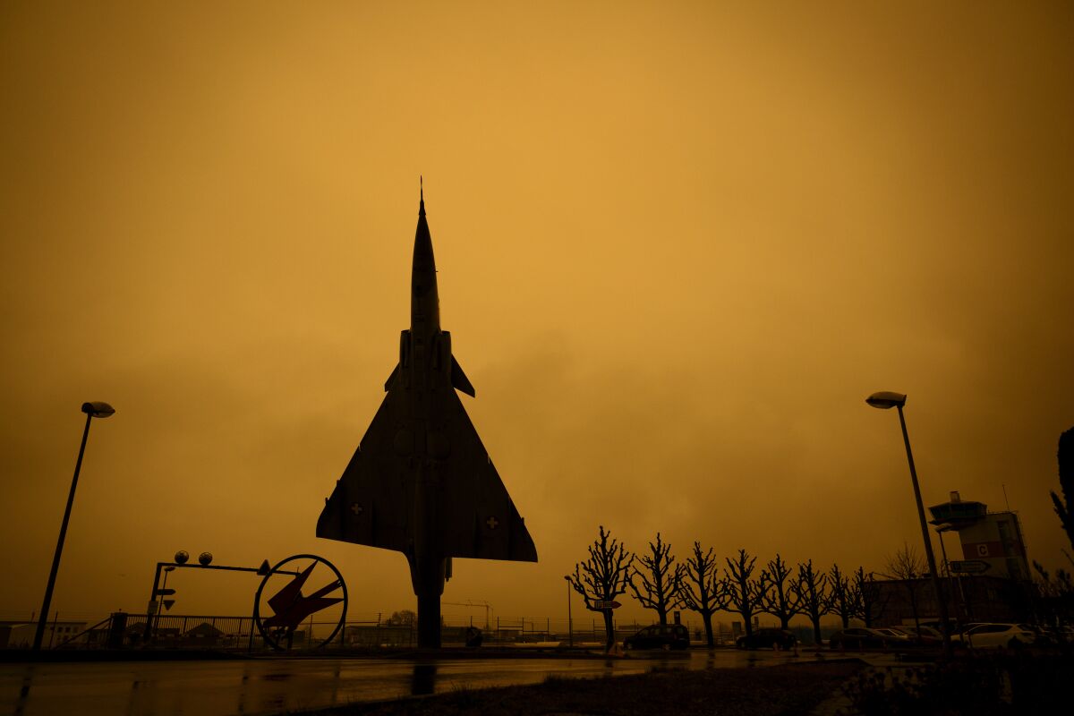 A former Swiss Air Force jet fighter Mirage 2000 manufactured by Dassault Aviation is placed on display in front of the entrance of the Swiss Army at Payerne Air Base as Sahara sand colours the sky in orange and creates a special light atmosphere, Switzerland, Tuesday, March 15, 2022. A huge dust storm is swirling over Europe from the Sahara desert. (Laurent Gillieron/Keystone via AP)