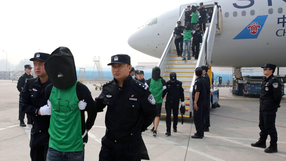 In this photo released by Xinhua News Agency, Chinese suspects involved in wire fraud are escorted off a plane after arriving at the Beijing Capital International Airport on April 13, 2016. (Yin Gang / AP)