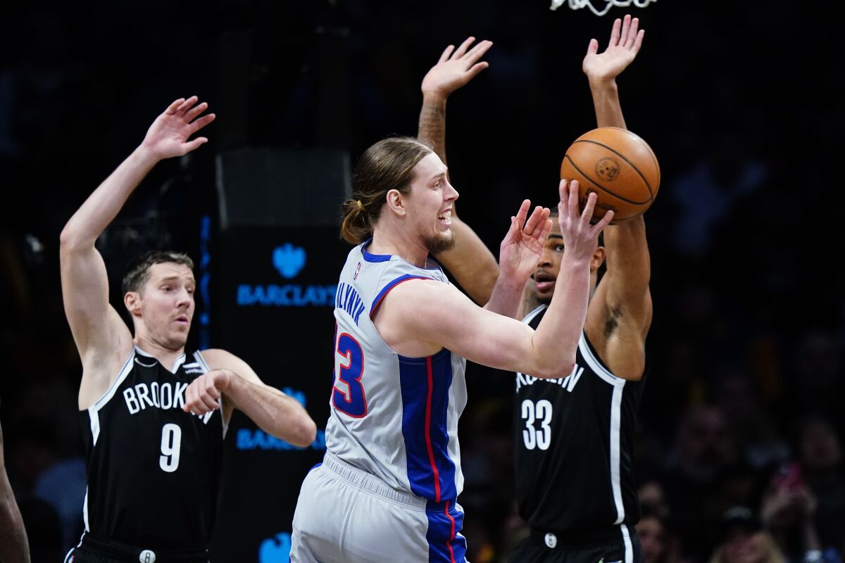 Detroit Pistons' Kelly Olynyk (13) passes away from Brooklyn Nets' Nic Claxton (33) and Goran Dragic (9) during the second half of an NBA basketball game Tuesday, March 29, 2022 in New York. The Nets won 130-123. (AP Photo/Frank Franklin II)
