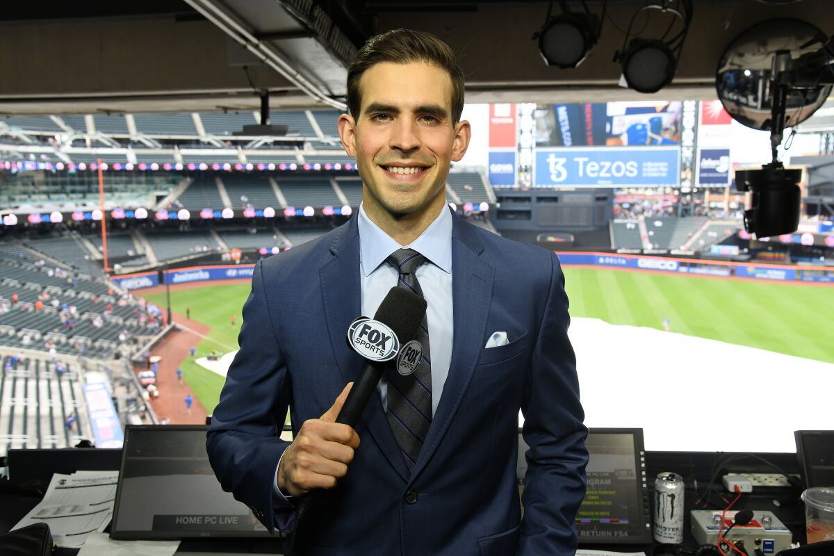 Joe Davis holds a Fox Sports microphone and smiles from inside a TV booth