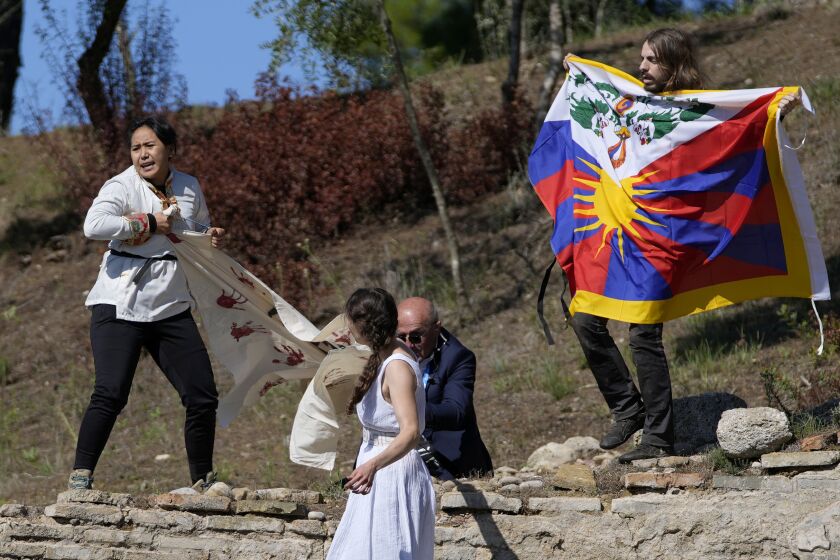 A police officer tries to stop protesters displaying a Tibetan flag and a banner reading "No genocide games" during the lighting of the Olympic flame at Ancient Olympia site, birthplace of the ancient Olympics in southwestern Greece, Monday, Oct. 18, 2021. The flame will be transported by torch relay to Beijing, China, which will host the Feb. 4-20, 2022 Winter Olympics. (AP Photo/Thanassis Stavrakis)