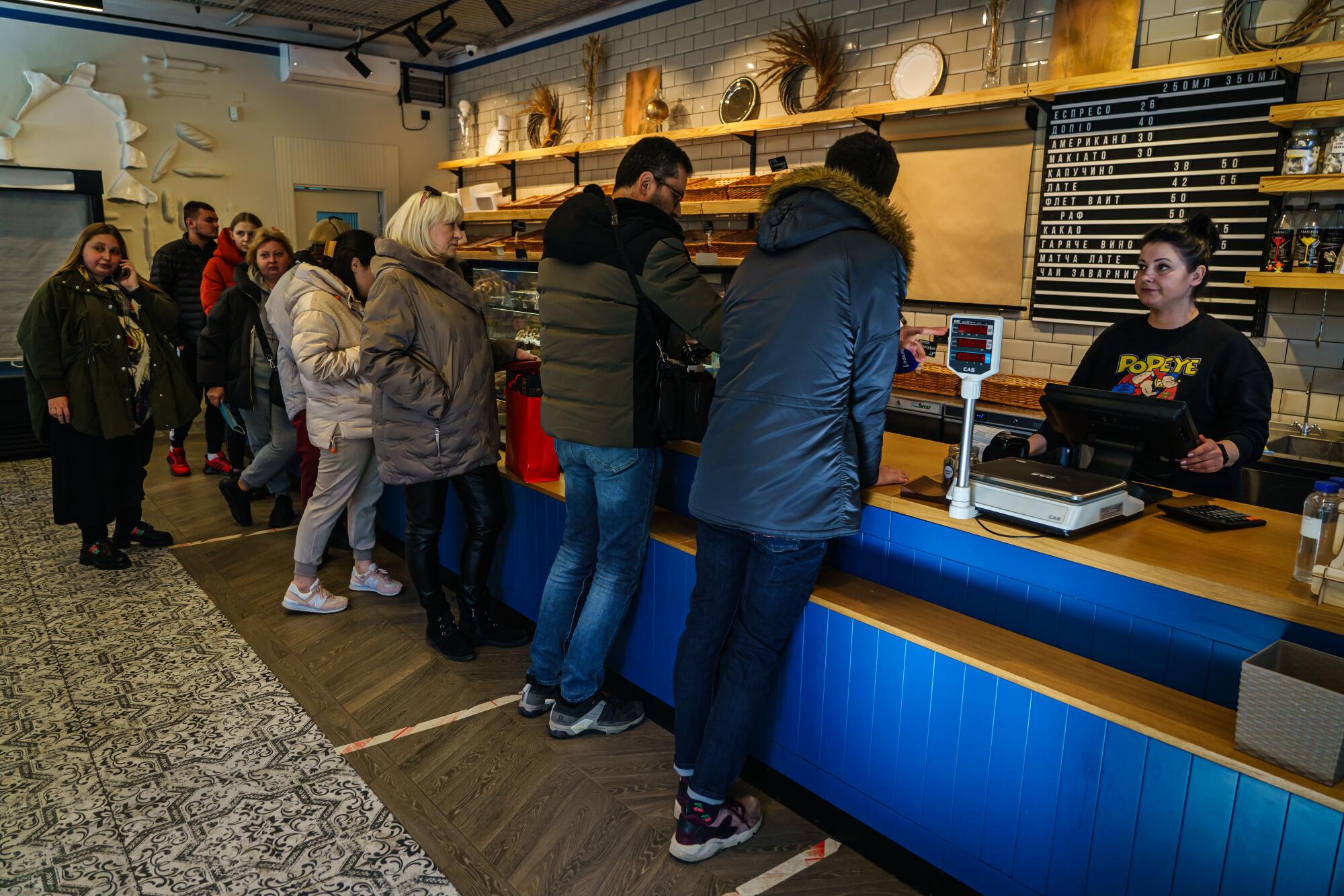 Customers in coats wait at a pastry shop.