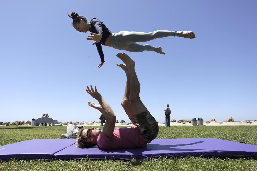 San Diego, CA_5_6_24_Kylee Baze, top, is propelled into the air by acroyoga partner Nicholas "Modern Tarzan" Coolidge on the grass near the main lifeguard tower in Ocean Beach Monday afternoon. "We're loving the new grass," said Baze about the condition of the park. Photo by John Gastaldo for the Union-Tribune