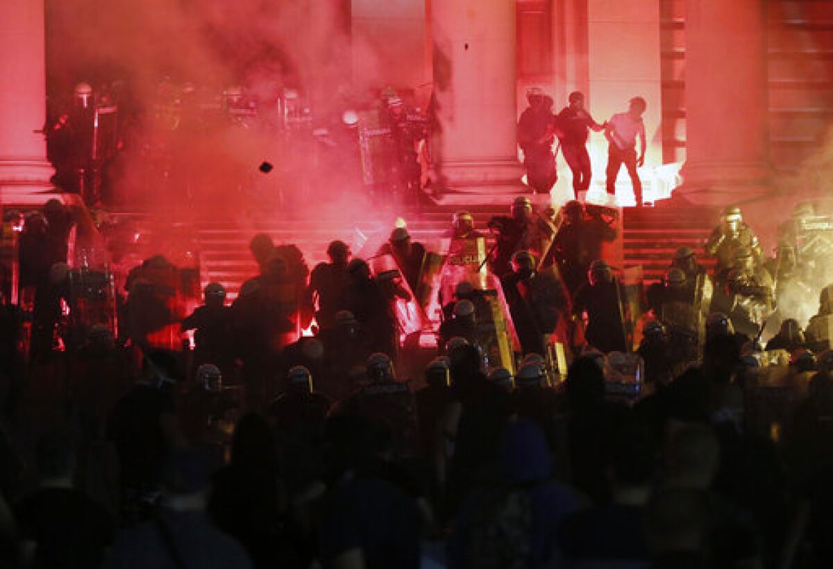 Protesters clash with riot police on the steps of the Serbian parliament during a protest in Belgrade, Serbia, Friday, July 10 2020. Hundreds of demonstrators tried to storm Serbia's parliament on Friday, clashing with police who fired tear gas during the fourth night of protests against the president's increasingly authoritarian rule. The protests started on Tuesday when President Aleksandar Vucic announced that Belgrade would be placed under a new three-day lockdown following a second wave of confirmed coronavirus infections. (AP Photo/Darko Vojinovic)