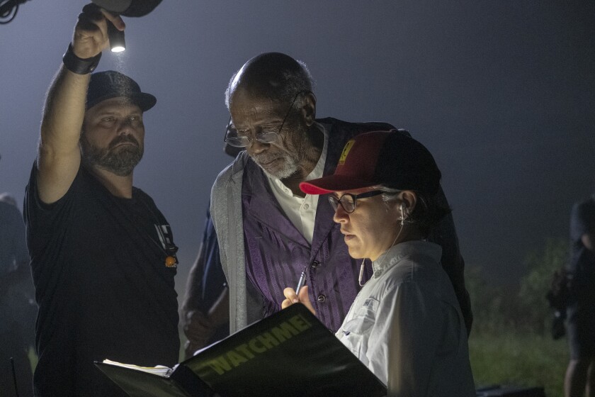 Louis Gossett Jr. and Nicole Kassell look at a binder she’s holding with “WATCHMEN” on the cover while another man shines a flashlight.