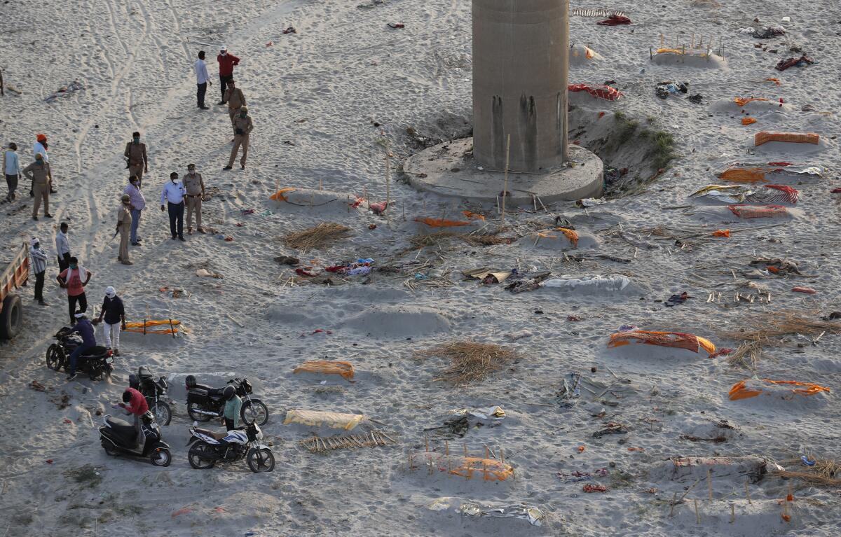 An aerial view of people standing, and motorcycles parked, on sand amid scattered, lightly covered mounds.