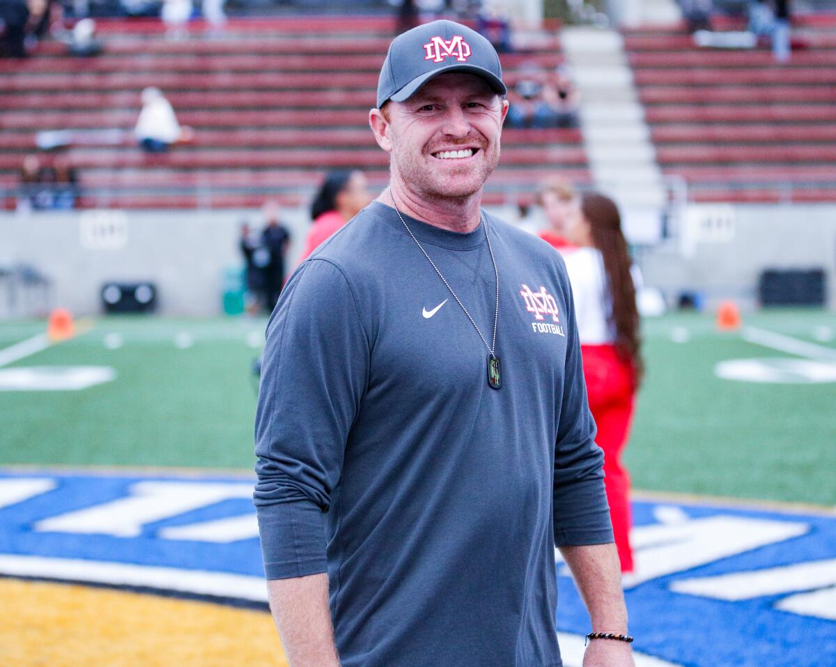 Mater Dei first-year coach Frank McManus stands on a football field and smiles.