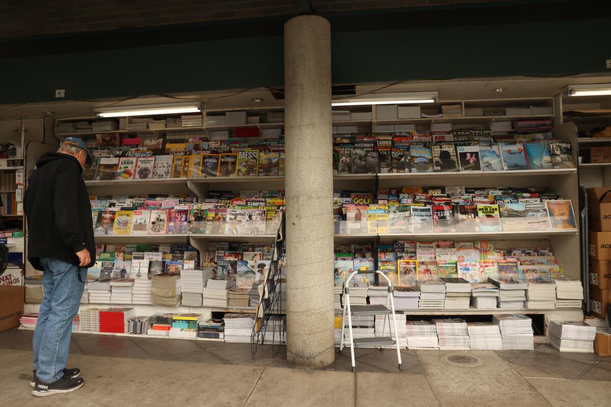 A man stops by the Above the Fold newsstand near rows of periodicals.