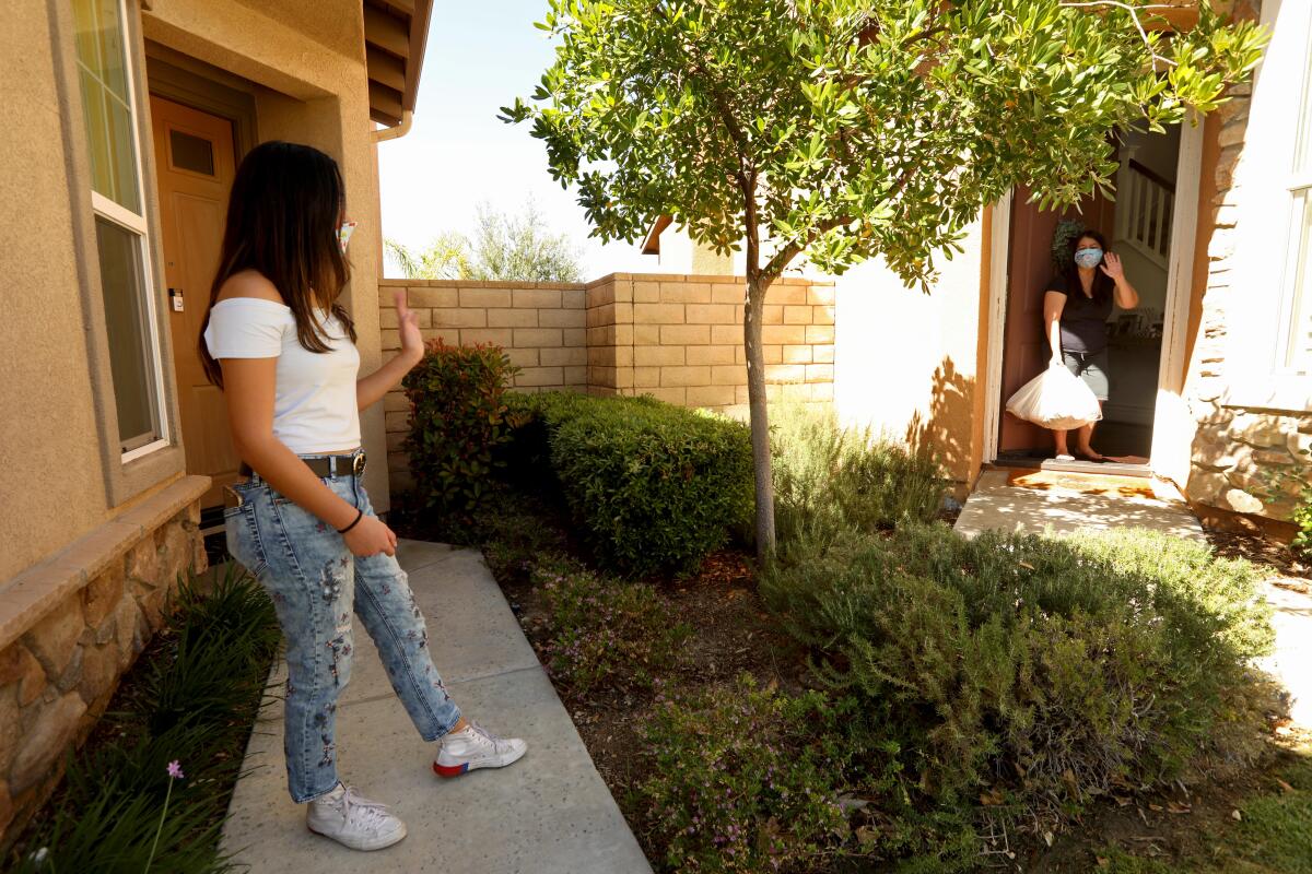 Sharia Busnawi, 16, left, a junior at West Ranch High School, waves to Joanne Halcon, who thanked the teen for delivering groceries to her home in Santa Clarita on Tuesday.