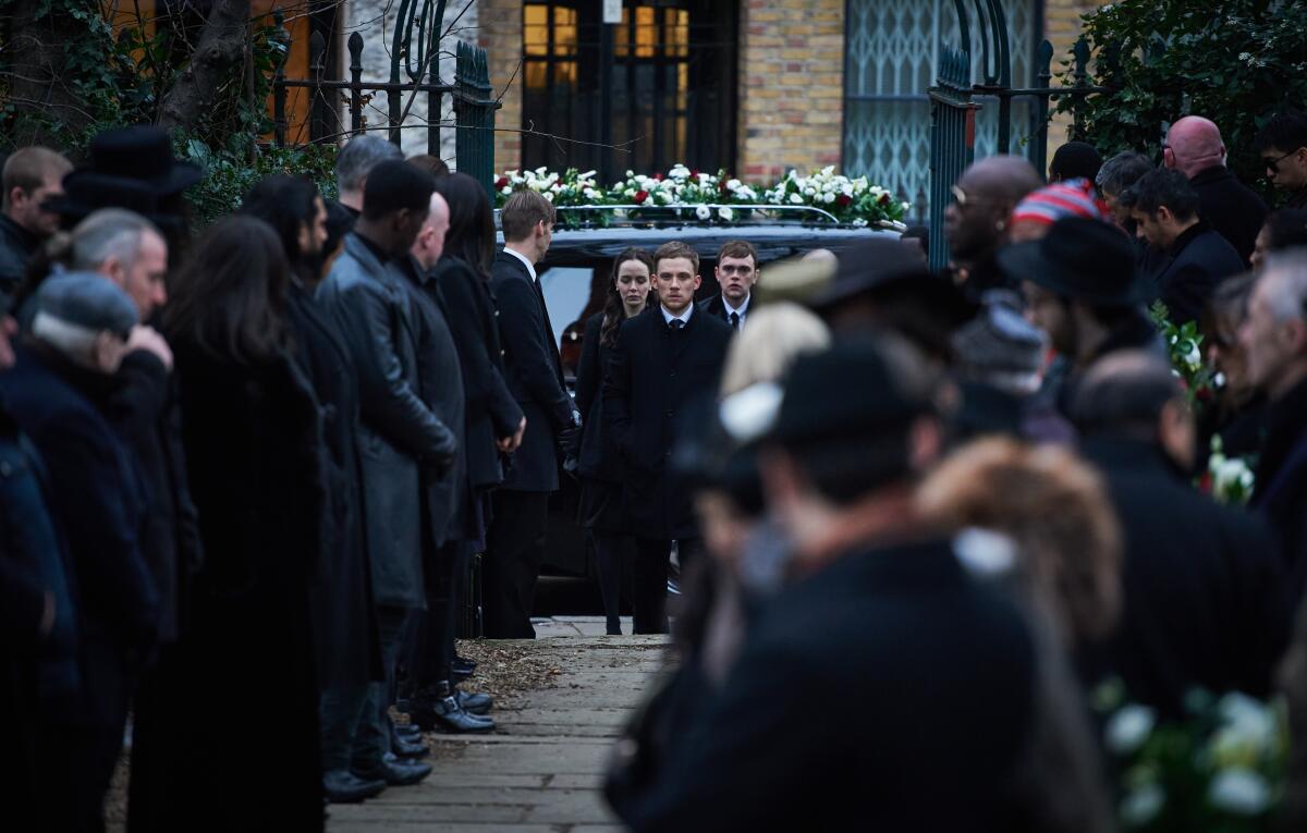 A man leads a funeral procession through a crowd. 