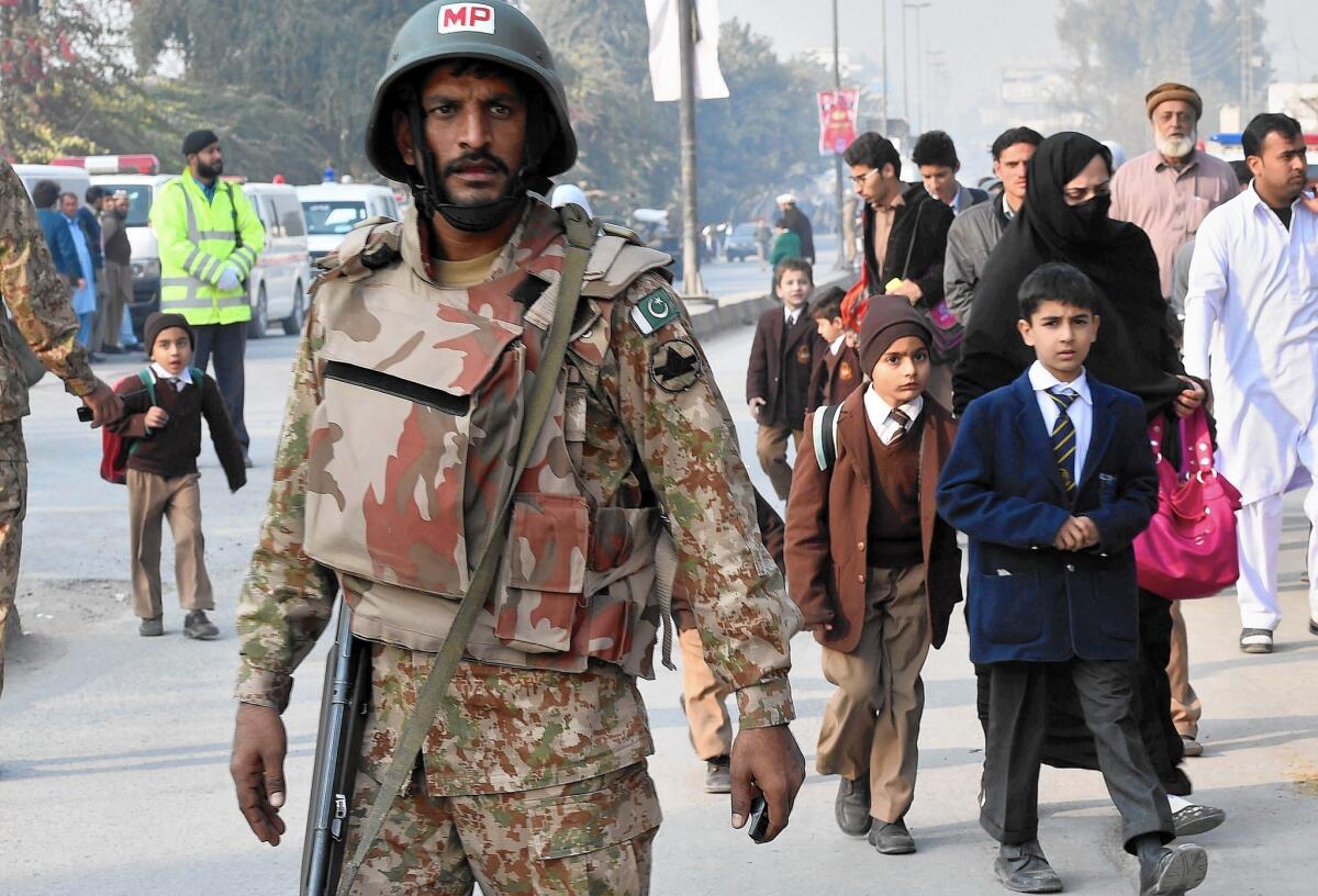 A Pakistani soldier stands guard as parents leave with their children near the site of an attack by Taliban gunmen on a school in Peshawar on Dec. 16.