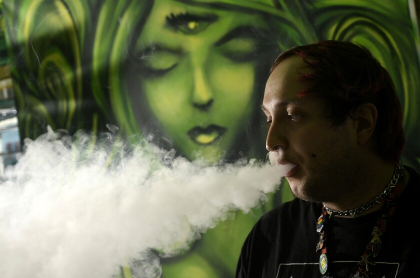 A man blows smoke while sitting in front of a green artwork