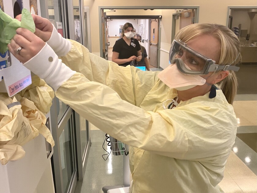 یک زن در حین کمبود پرسنل در مرکز پزشکی سنت چارلز در بند ، اور ، تجهیزات حفاظتی می پوشد.