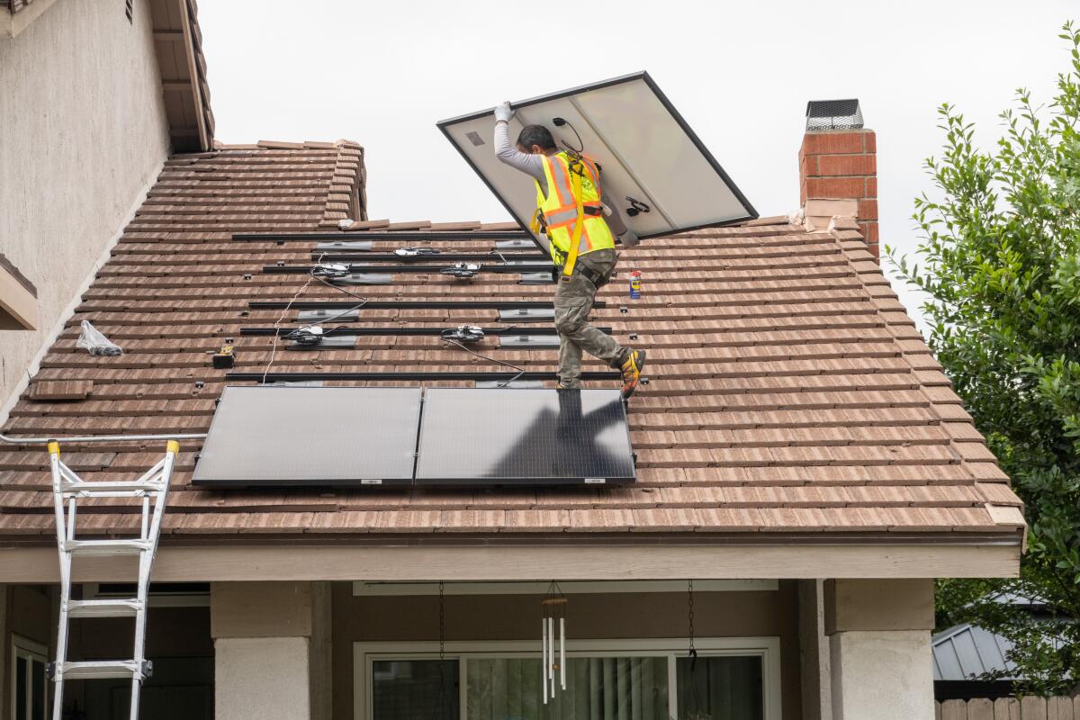 An installer carries a solar panel on a roof 
