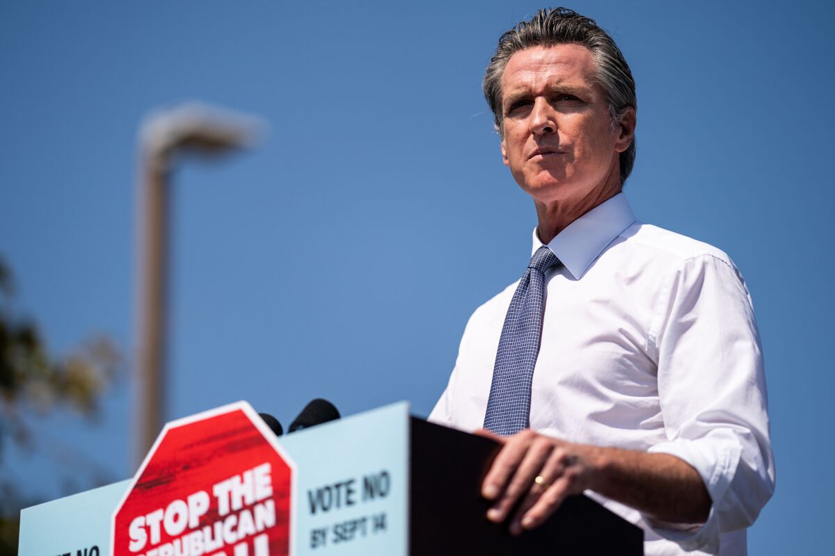 Newsom stands at a lectern with a "Stop the Republican recall" sign.