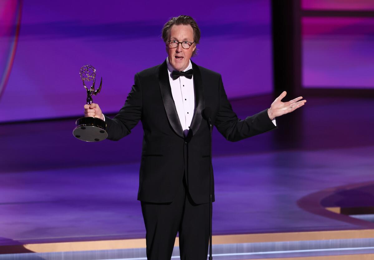 A man in a tuxedo holding an Emmy with his arms extended.