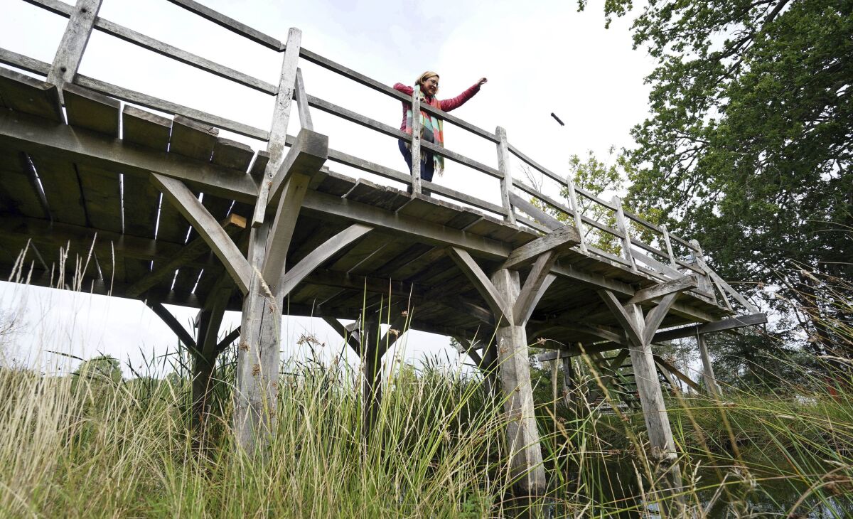 Silke Lohmann of Summers Place Auctions stands on the original Poohsticks Bridge from Ashdown Forest, featured in A.A. Milne's Winnie the Pooh books and E.H. Shepard's illustrations, near its original location in Tonbridge, Kent, England, Thursday, Sept. 30, 2021. The adventures of the honey-loving bear “Winnie the Pooh” have captivated children and their parents for nigh on 100 years. Fans now have a chance to own a central piece of Pooh’s history, when a countryside bridge from the south of England goes up for auction next week. The author of the hugely popular Pooh series of books, A. A. Milne, often played with his son, Christopher Robin, at the bridge in the 1920s. The bridge became a regular setting for the adventures of Pooh and his friends in the series that launched in 1926. The auctioneers have said there’s been interest from around the world, but hoped that it stays local. (Gareth Fuller/PA via AP)