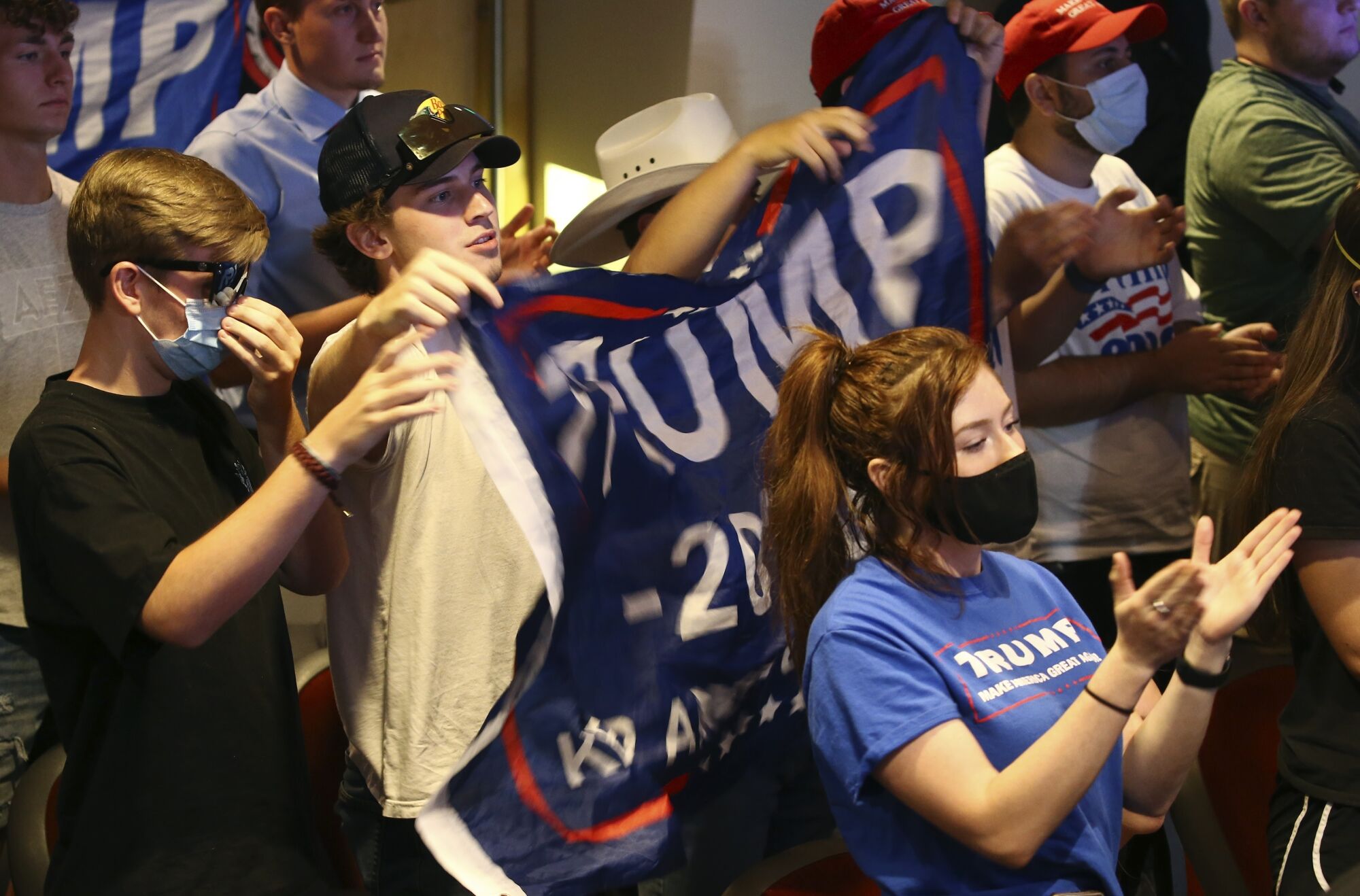 Young people, some of whom are masked, hold up a campaign banner bearing the word Trump 