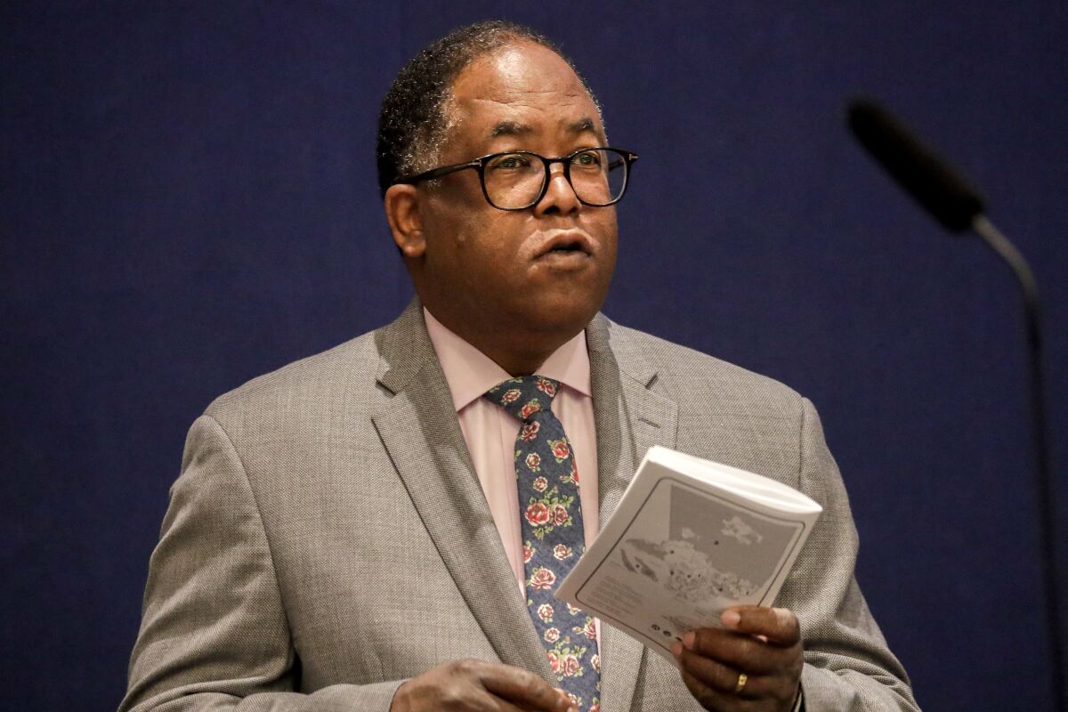 Mark Ridley-Thomas in a gray suit holding a pamphlet while speaking into a microphone