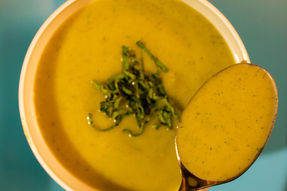 A spoon full of orange soup held above a bowl of the soup with green garnish