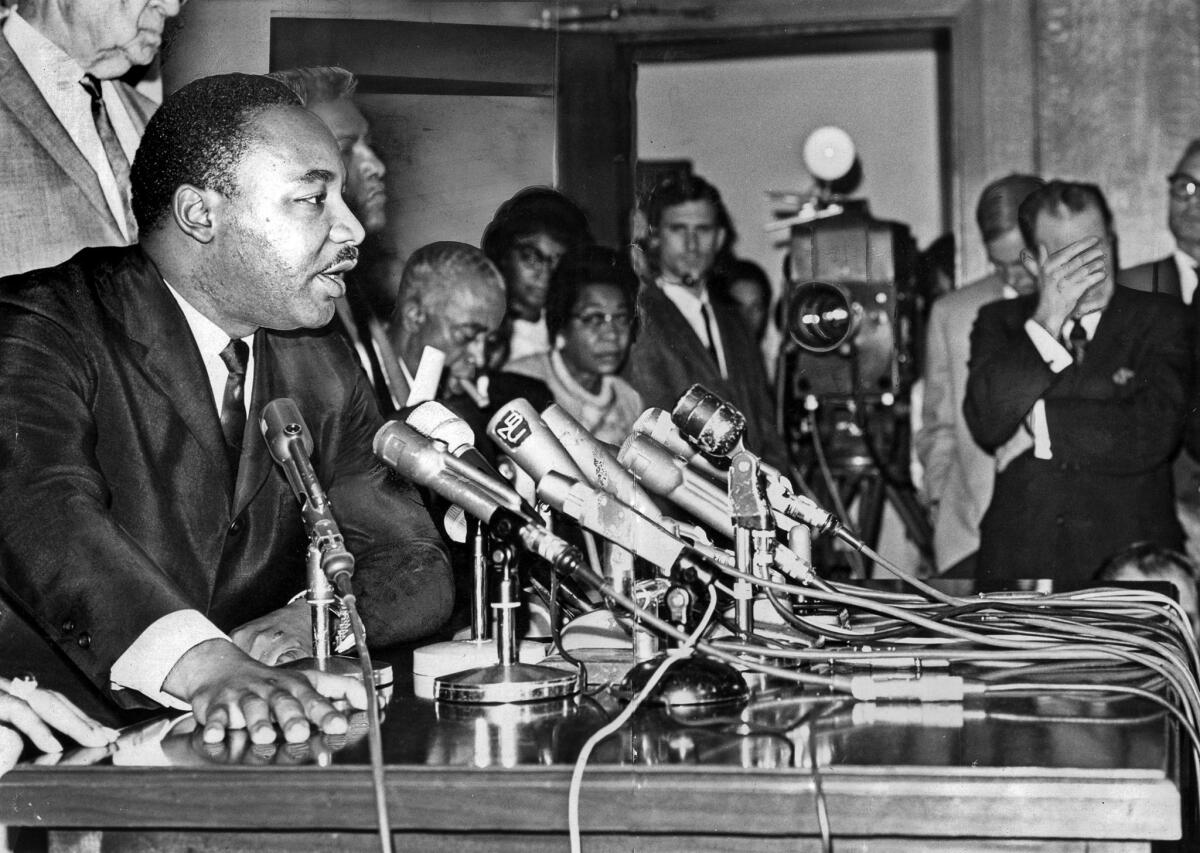 Aug. 19, 1965: The Rev. Martin Luther King Jr. answers questions during a news conference at Los Angeles City Hall. Mayor Sam Yorty, right, listens with his hand covering his eyes.