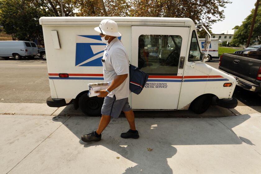San Pedro, California,-Aug. 20, 2020-A Los Angeles county postal carrier delivers mail on Aug. 20, 2020. United States Postal Workers were offered 12 weeks of leave due to the coronavirus pandemic, which caused a backlog of mail that needed to be delivered. Many postal carriers were offered overtime. A lack of enough postal carriers is one of the reasons that the United States Postal Service is behind on delivering mail. (Carolyn Cole/Los Angeles Times)