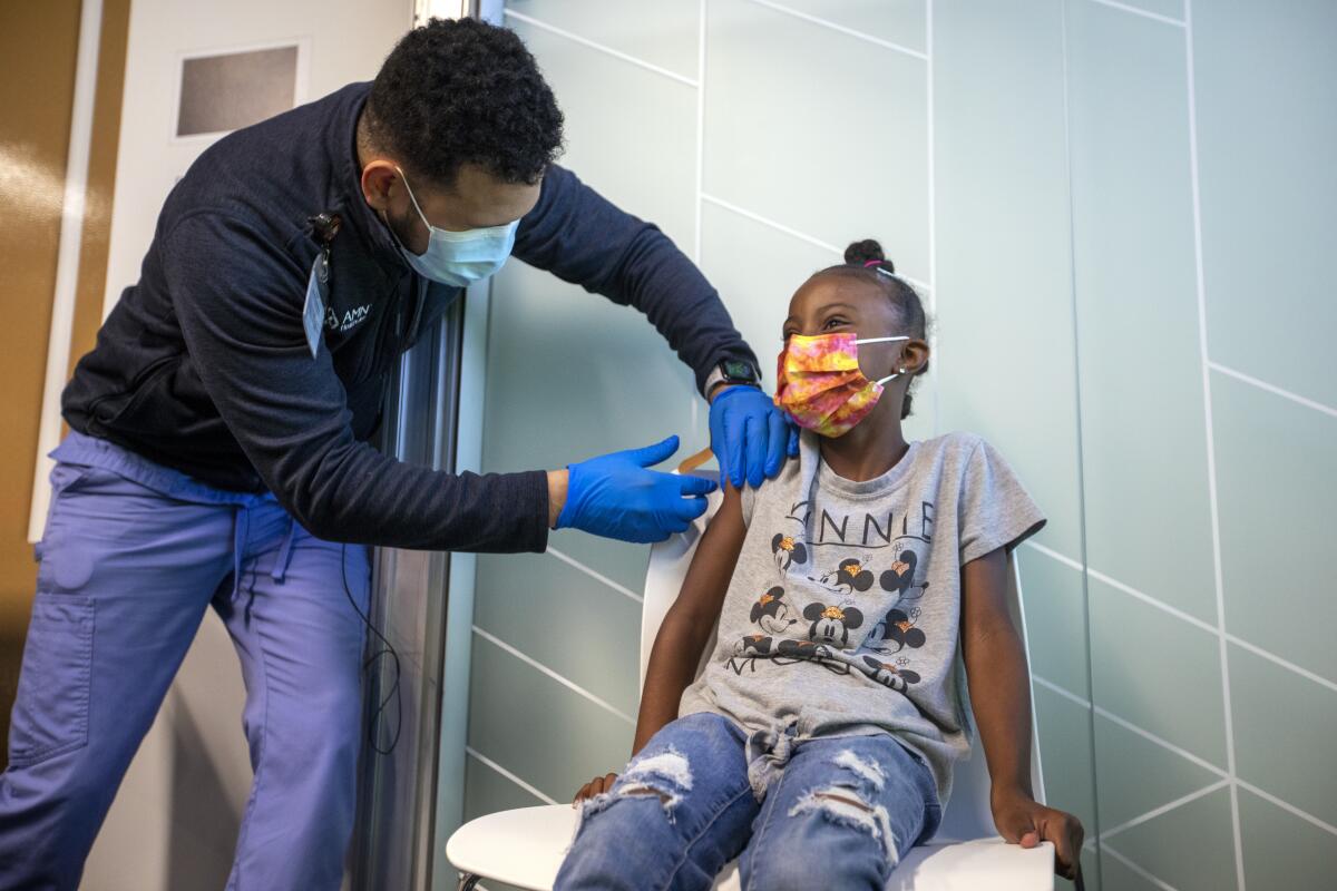 A man administers a vaccine shot to a girl sitting in a chair