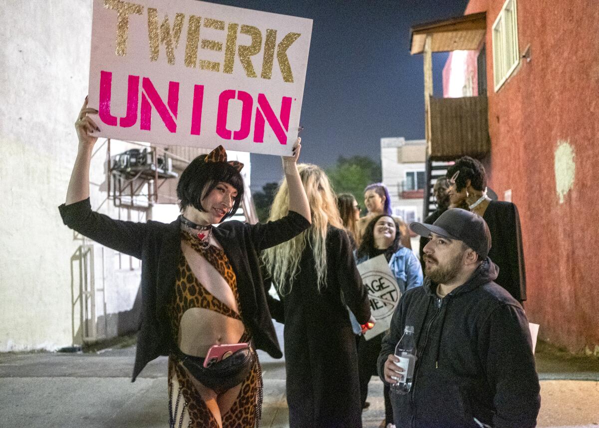 A person at left holds up a 'Twerk Union' sign while talking to another person outside in the evening.