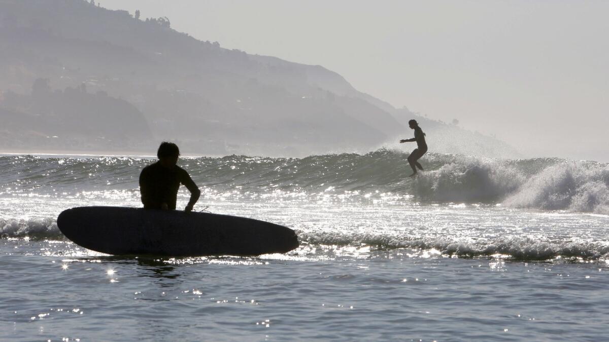 MALIBU, CA- July 6, 2018: Sun sparkles off the ocean as a surfer rides a wave at Surfrider Beach in Malibu. The first heat wave of the summer hit the area today, sending temperatures into triple-digit territory. The high in Malibu today is predicted to be 101 degrees. (Katie Falkenberg / Los Angeles Times)