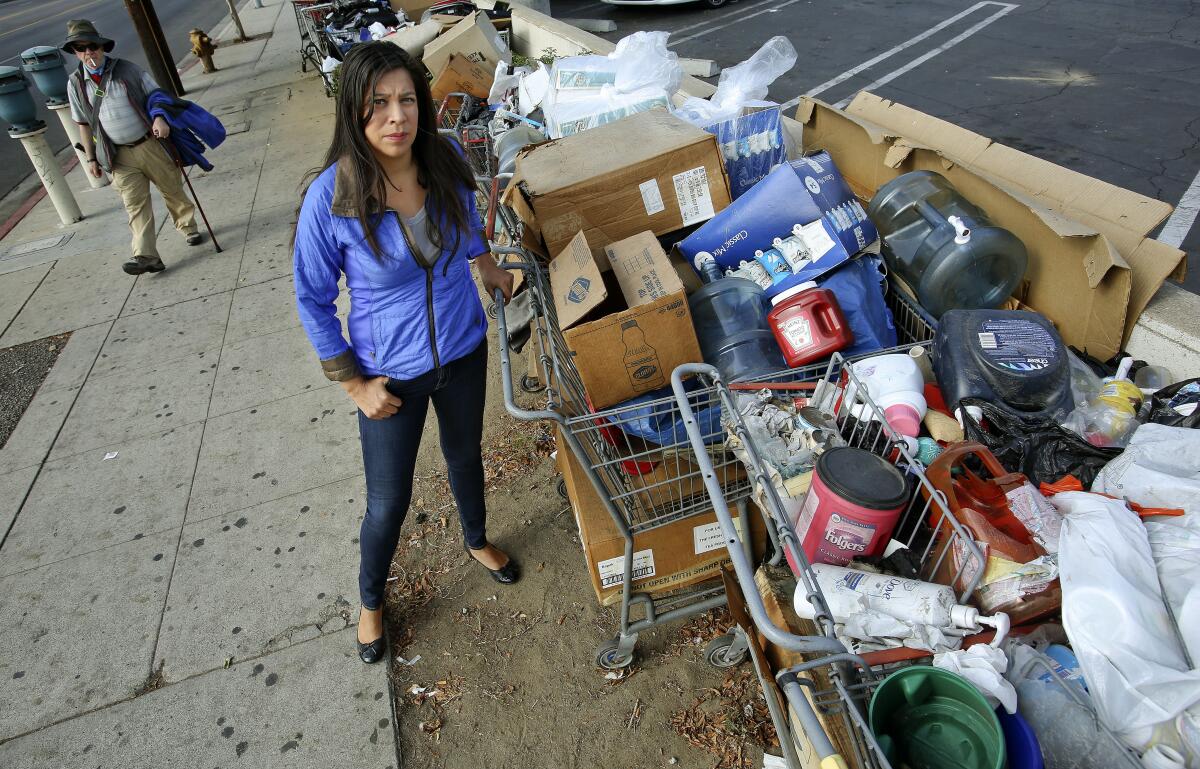 A woman stands next to a row of shopping carts filled with boxes and trash bags.