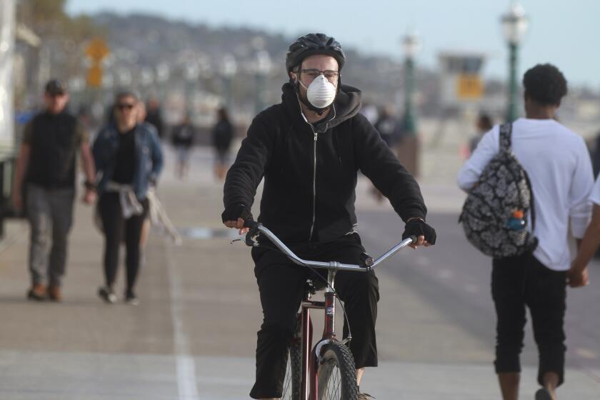 A 35-year-old Mission Hills resident, who said his name was Michael, no last name given, wears a mask as a precaution for the coronavirus as he rides his bike on the Mission Beach Boardwalk on Friday, March 20, 2020 in San Diego, California.