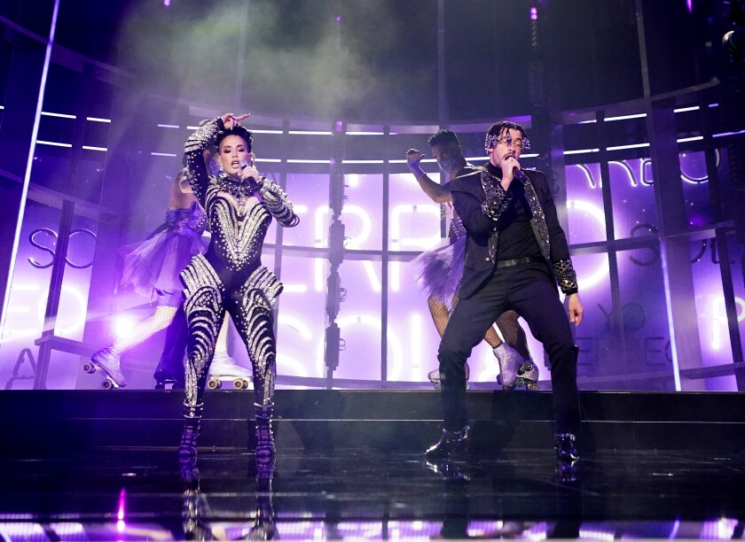 A woman and a man hold microphones and sing onstage.