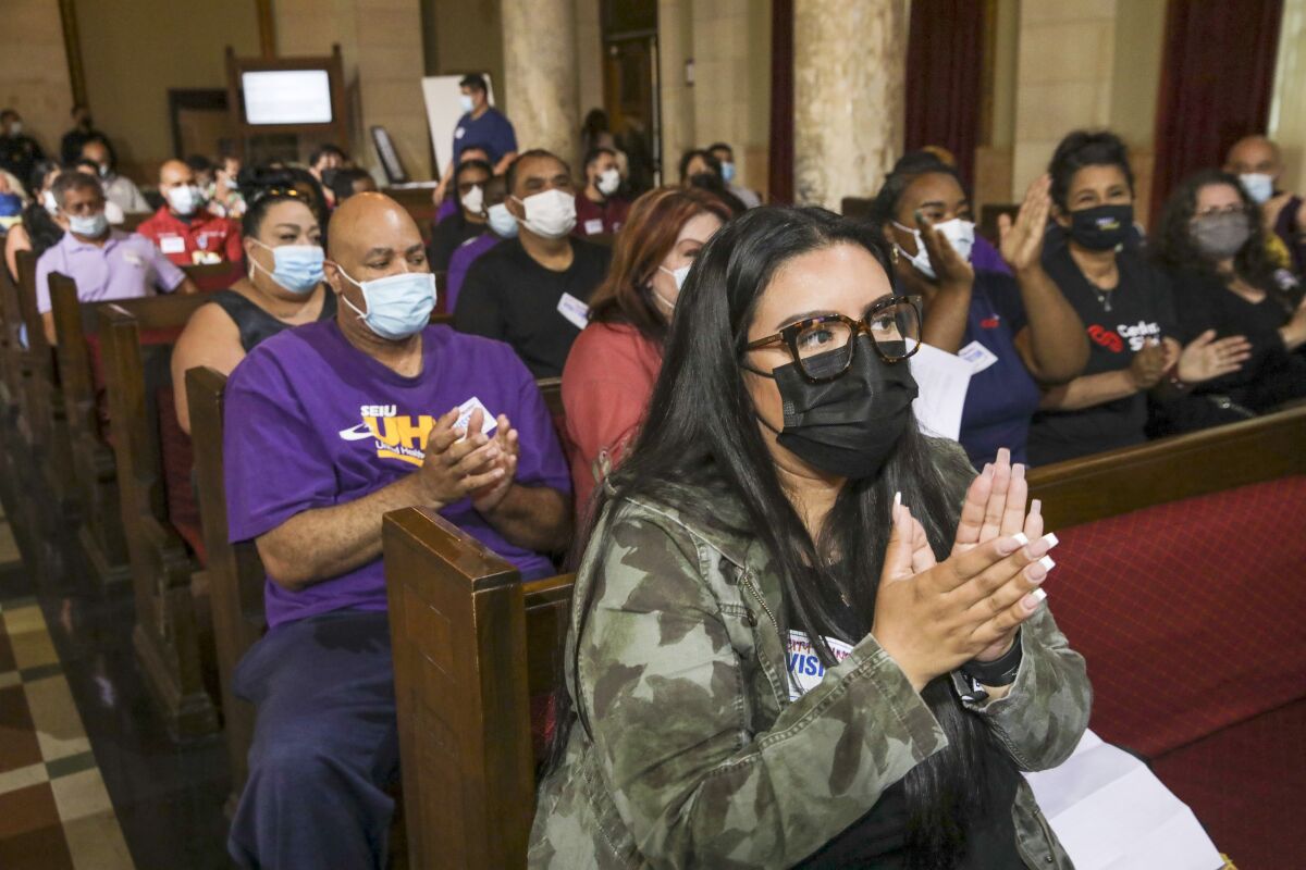 A roomful of people claps after the passage of an ordinance to boost the minimum wage for private hospital workers