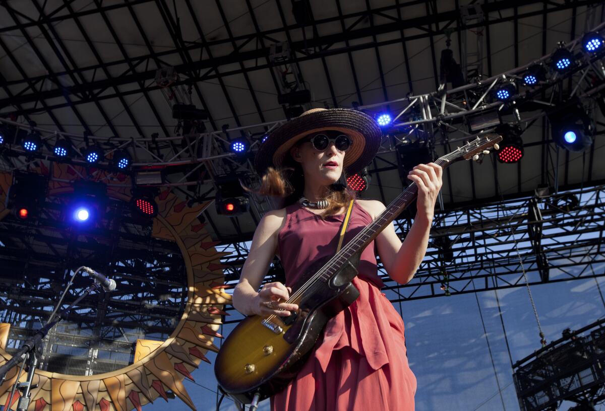 A woman in a hat and red dress plays a guitar on an outdoor stage