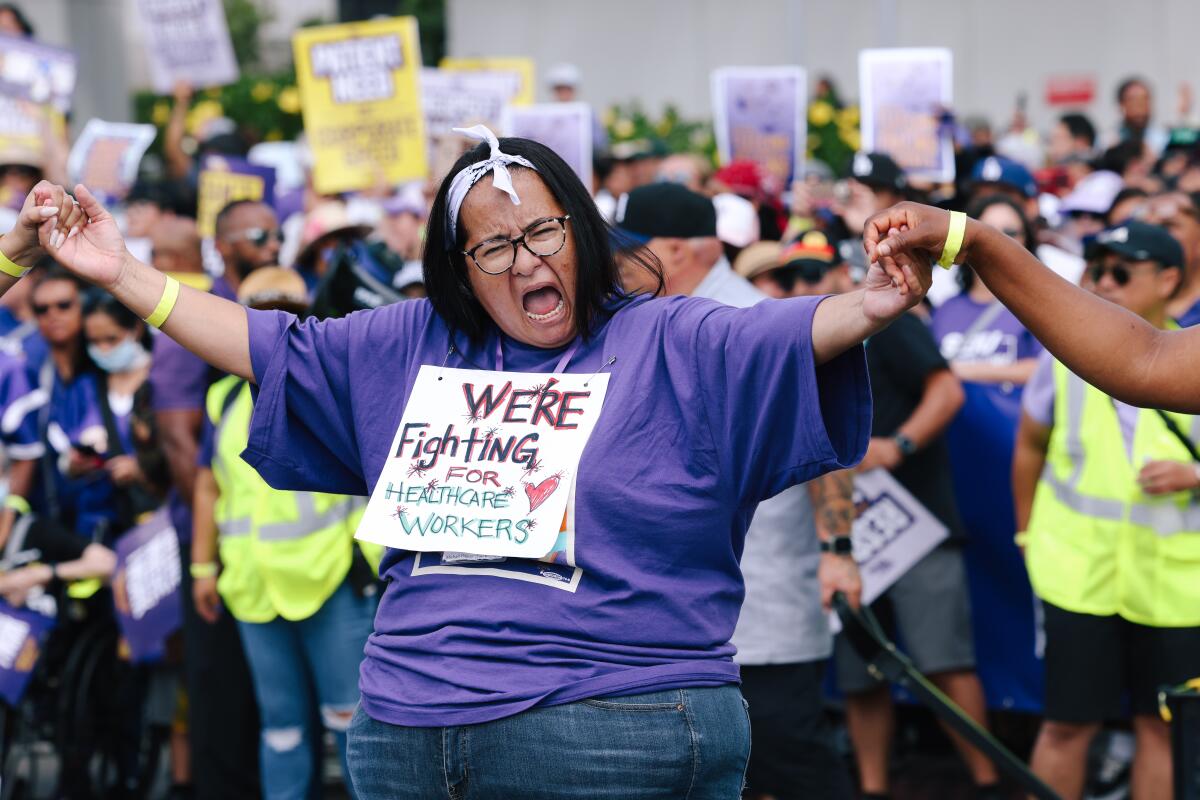 A woman wears a handmade placard reading, "We're fighting for healthcare workers."