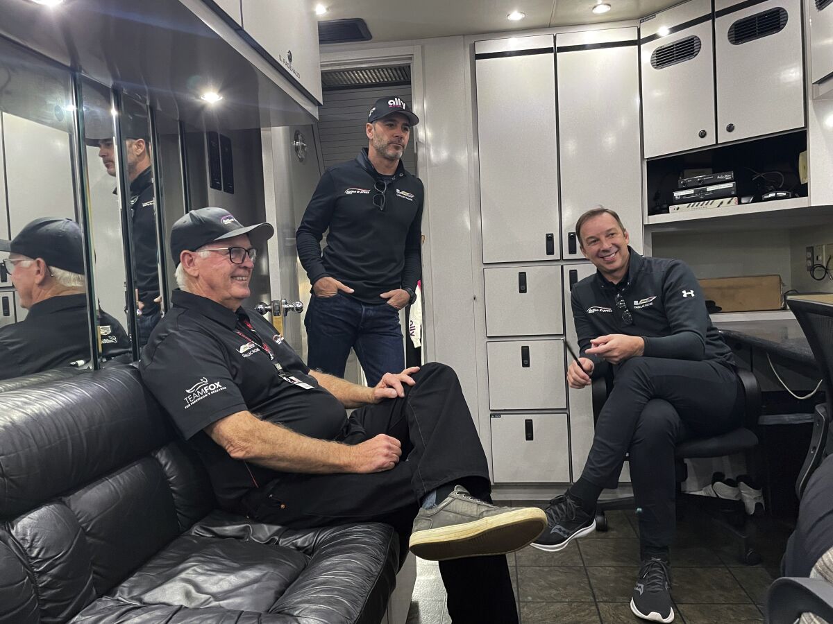 Seven-time NASCAR champion Jimmie Johnson stands in the doorway of the team hauler at Road Atlanta Raceway in Braselton, Georgia, Friday, Nov. 12, 2021, talking with Chad Knaus, right, his former crew chief, and Gary Nelson, team manager of the IMSA sports car Action Express Racing team. Johnson and Knaus have long had an on-and-off relationship that ended in 2019 after 17 seasons together. The two have been reunited by work four times this season as Knaus has run a sports car team that Johnson and Hendrick Motorsports put together in partnership with Action Express for four IMSA endurance sports car races this year. Both say their relationship is currently in a good place. (AP Photo/Jenna Fryer)