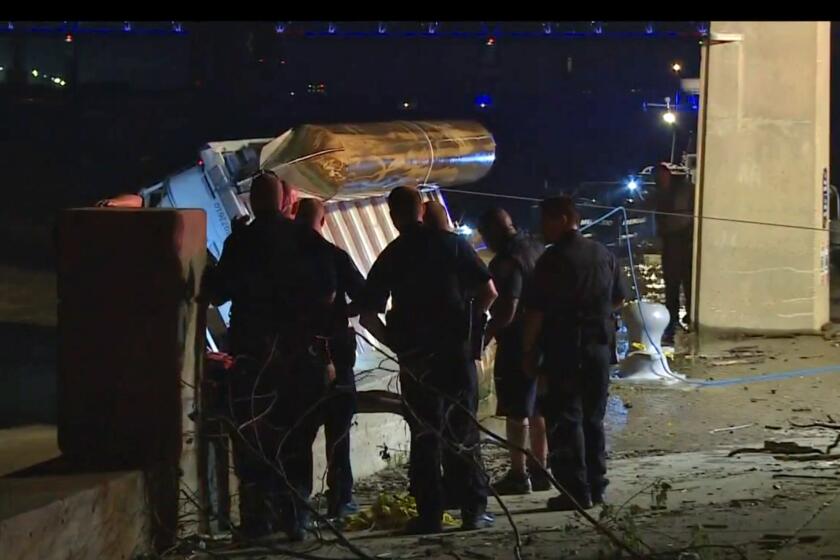 Police officers watch as an overturned pontoon boat is pulled from the Ohio River.