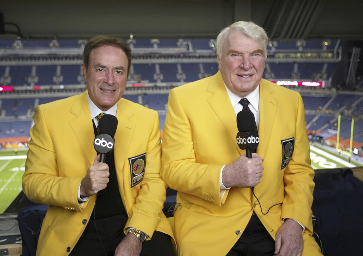 Two men seated side by side wearing yellow suit jackets with microphones in hand.