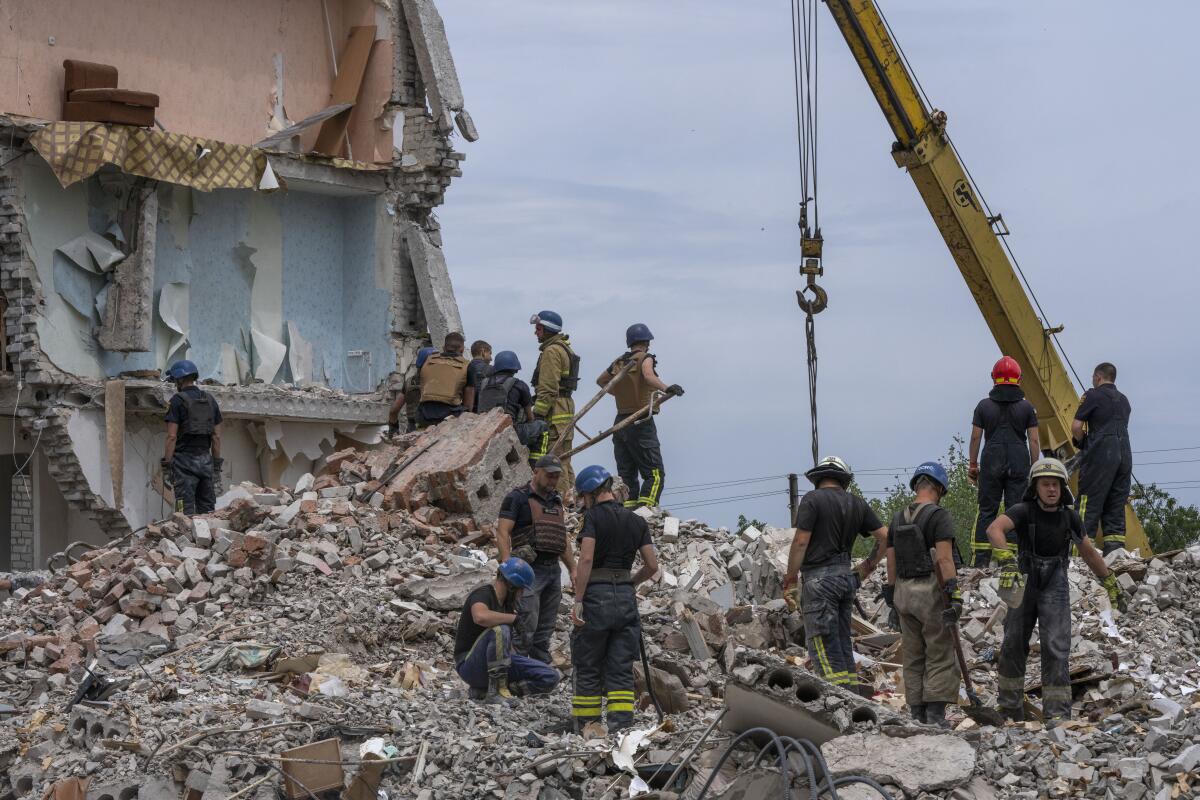 Rescue workers stand on the rubble at the scene in the aftermath of a missile strike in Chasiv Yar.