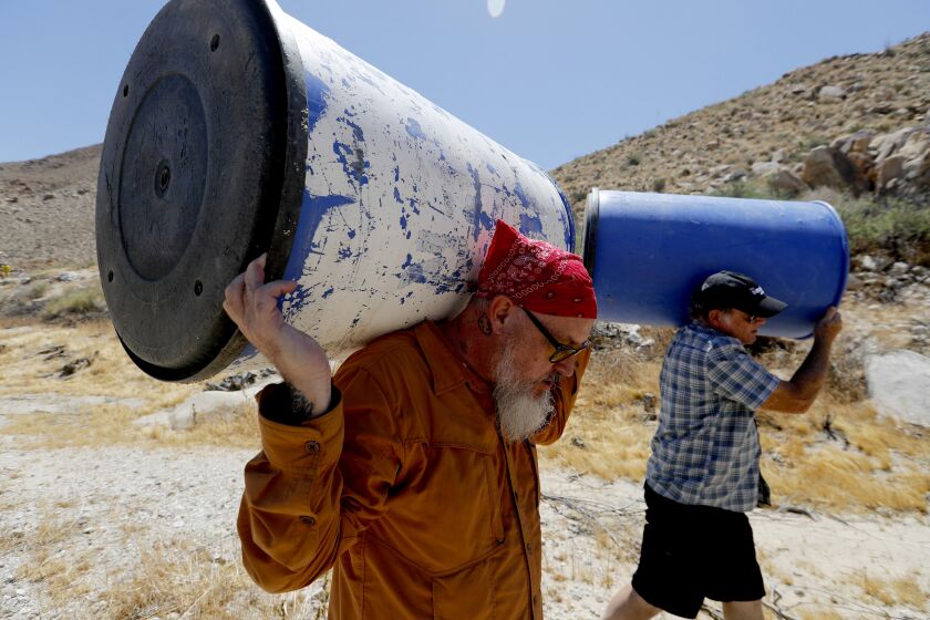 ANZA-BORREGO DESERT, CALIF. - JUNE 22, 2019. Water Station volunteers Brett Staulbaum ande Rob Fryer carry barrels into Carrizo Canyon in the Anza-Borrego Desert on Saturday, June 22, 2019. The barrels are used to store platic jugs of drininking water for thirsty migrants who have crossed the U.S.-Mexico border nearby. Founded by physicist John Hunter 20 years ago, the organization has water stations spread along the U.S.-Mexico border in California to help prevent migrants from dying of heat and dehydration as they make crossings in the barren and desolate area. (Luis Sinco/Los Angeles Times)