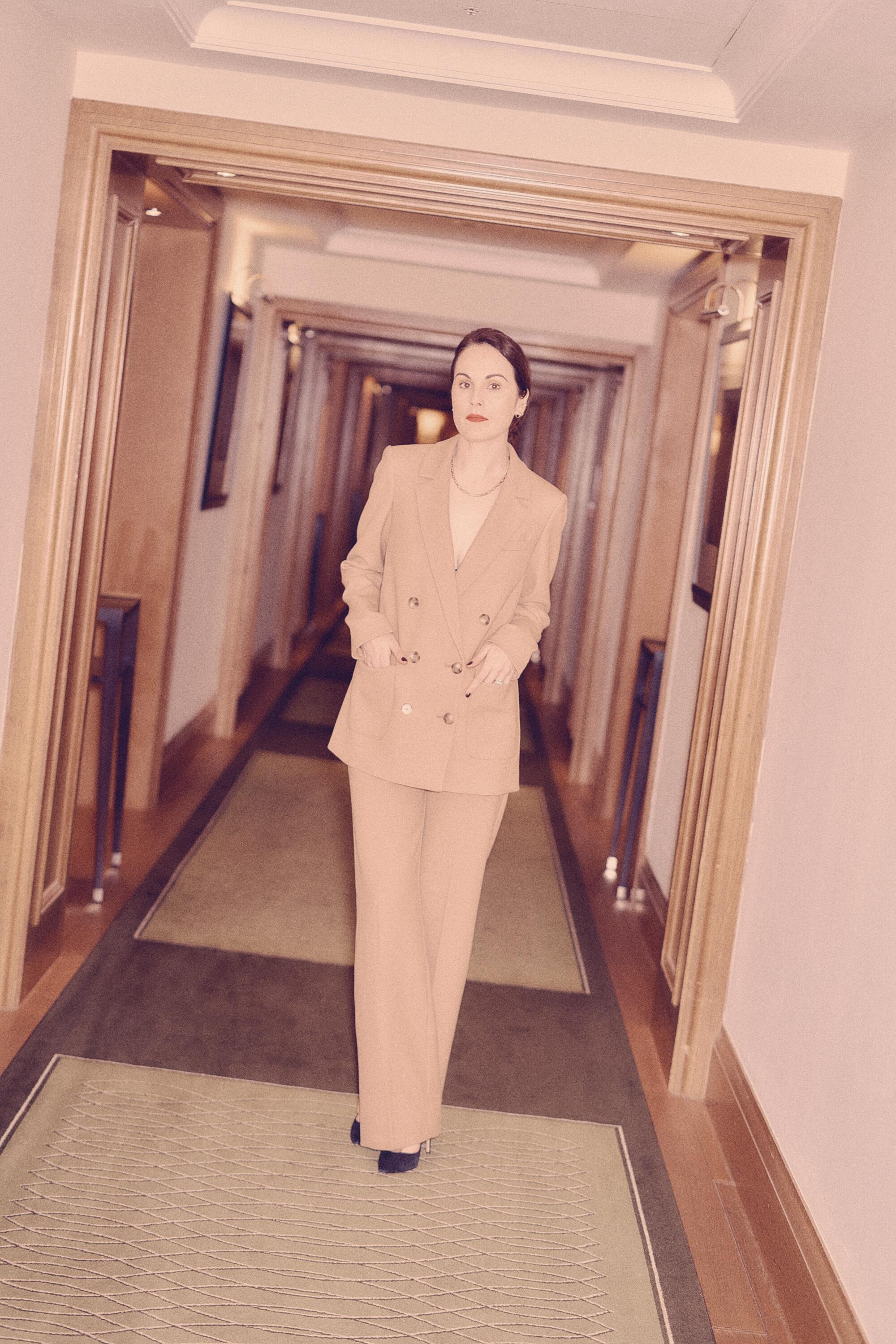 A woman in a suit poses in a hotel hallway.