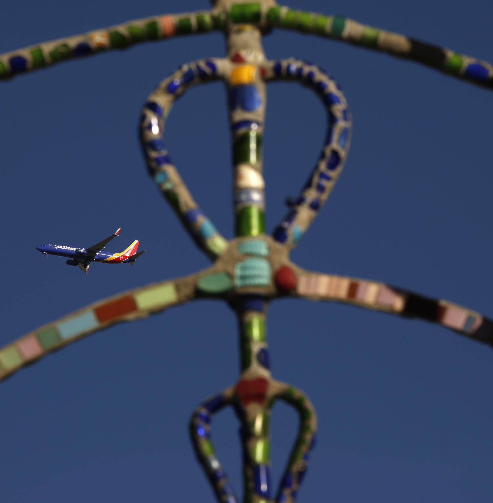 A plane in the air seen through a piece colorful metal artwork.